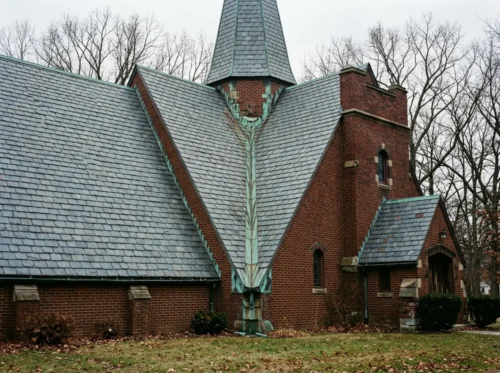 Steep grey slate roof on a brick church sanctuary with copper valley flashing